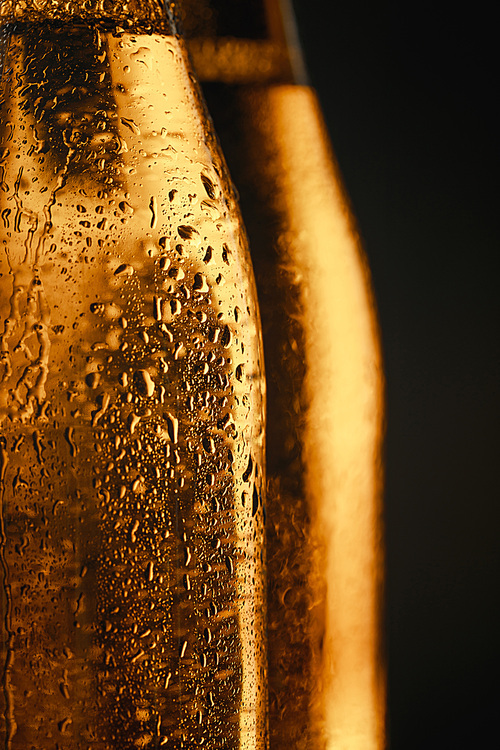 close up view of wet glass bottles of beer isolated on black