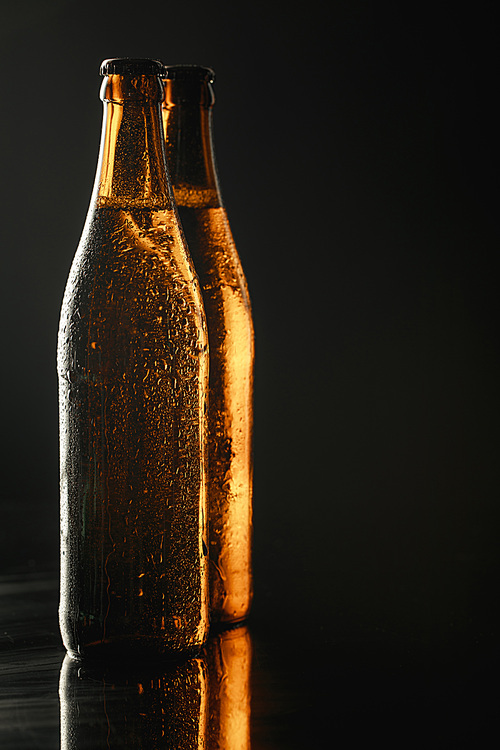 glass bottles of beer with drops isolated on black