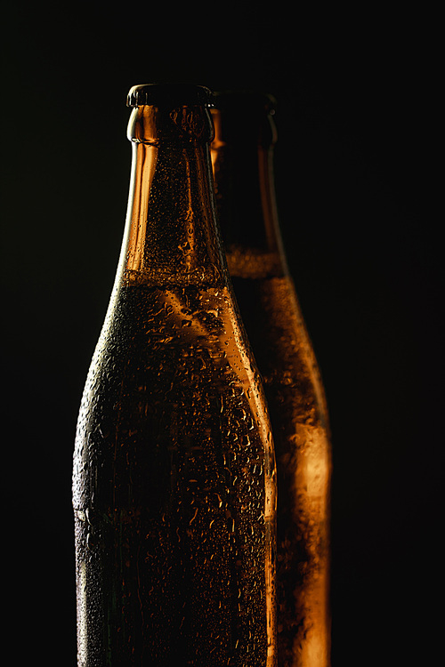 glass bottles of beer with water drops isolated on black