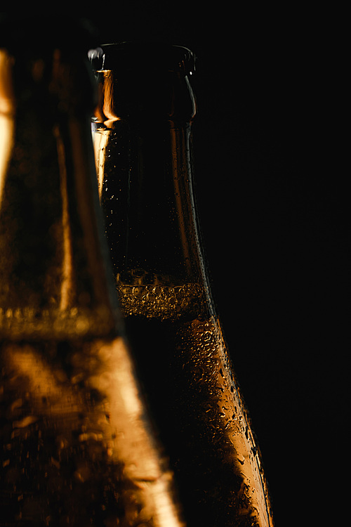 close up view of glass bottles of beer with water drops and bubbles isolated on black