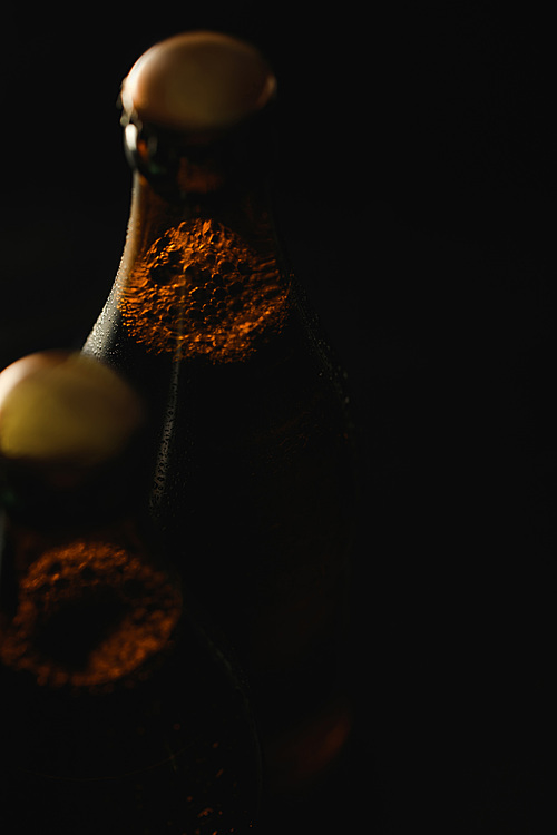 close up view of glass bottles of beer with bubbles isolated on black