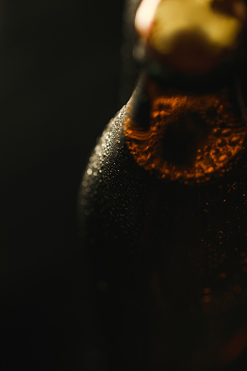 close up view of wet bottle of beer with bubbles isolated on black