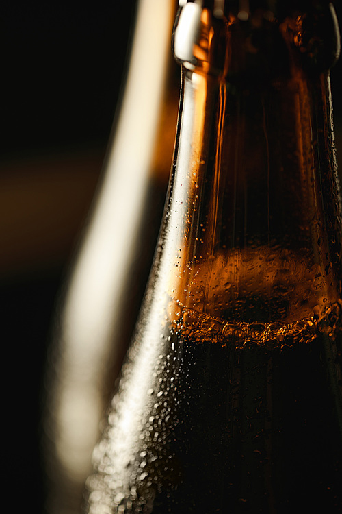close up view of wet brown bottle of beer with bubbles isolated on black