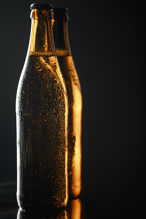 close up view of wet bottles of beer with drops isolated on black