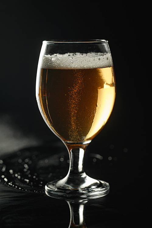 glass of beer with foam on wet surface isolated on black