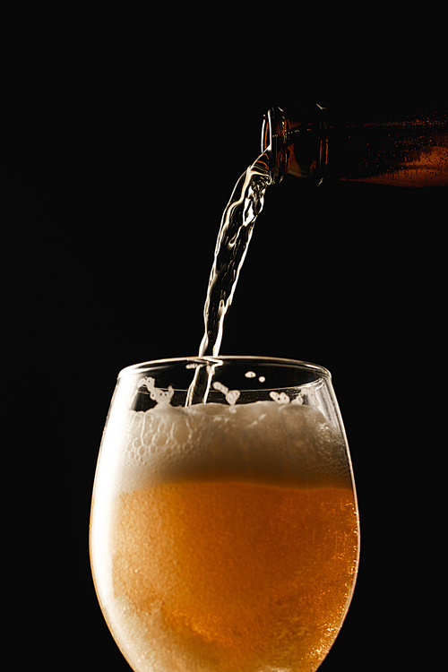 beer flowing from bottle into glass isolated on black