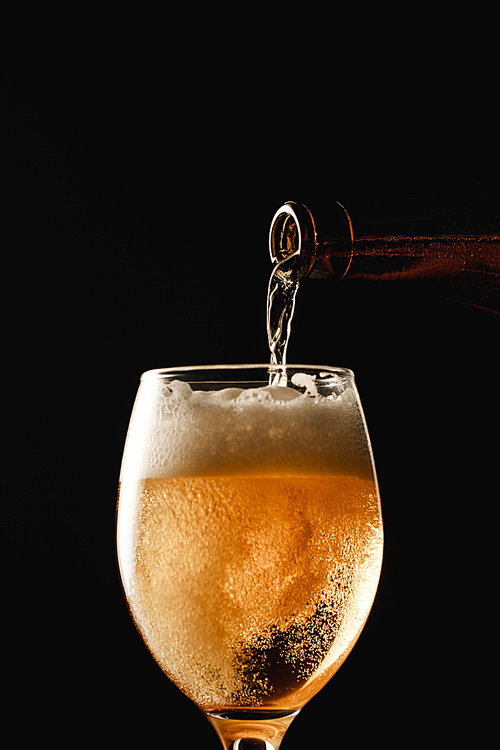 beer flowing from bottle into glass and making foam isolated on black
