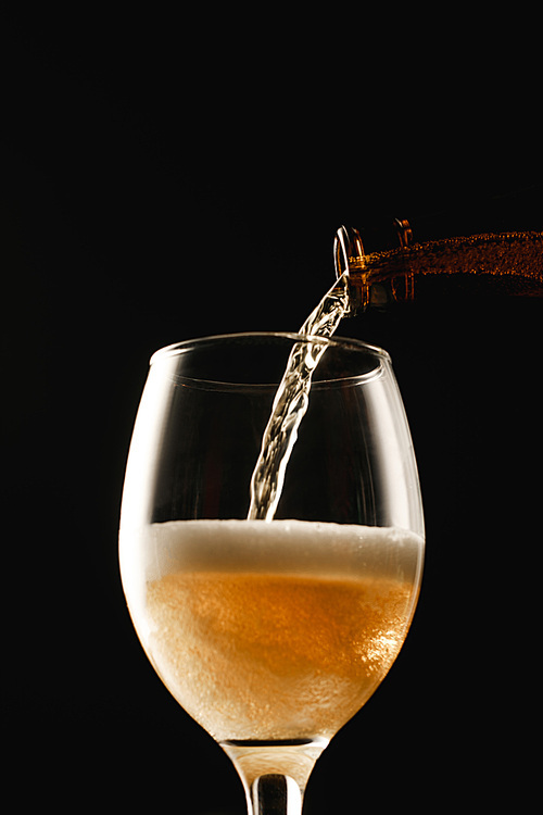 golden beer flowing from bottle into glass isolated on black