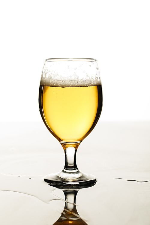 glass of beer with foam and puddle isolated on white