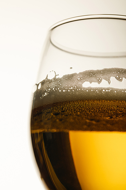 close up view of glass of beer with foam and bubbles isolated on white