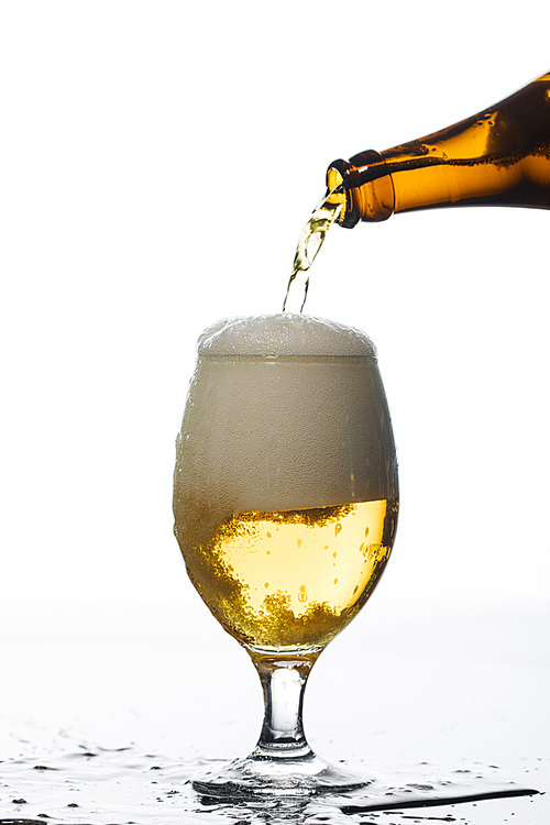 beer pouring from bottle into glass on surface with puddle isolated on white