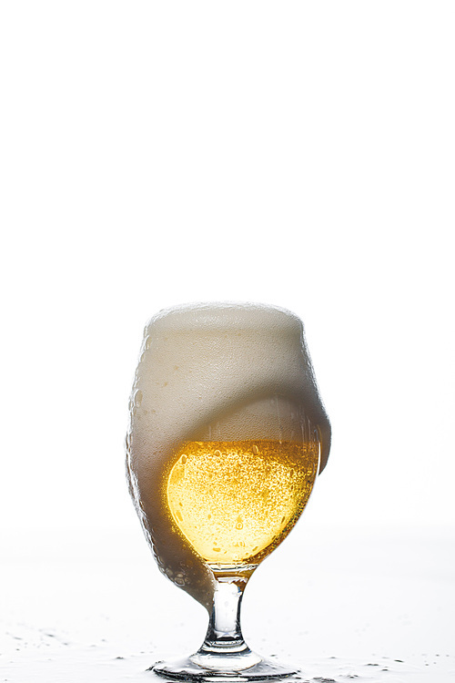 wet glass of beer with spilled foam isolated on white