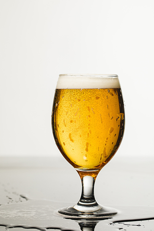 wet glass of beer with foam and puddle isolated on white