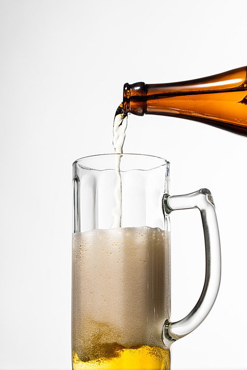 beer pouring from bottle into glass with foam isolated on white