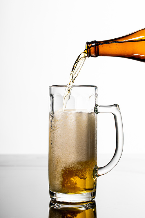 beer pouring from bottle into glass on table isolated on white