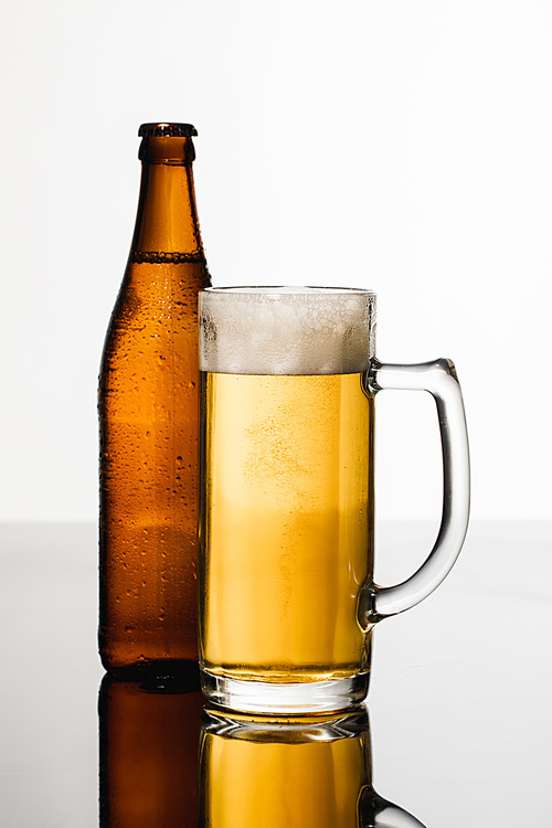 glass of beer with foam near wet bottle isolated on white