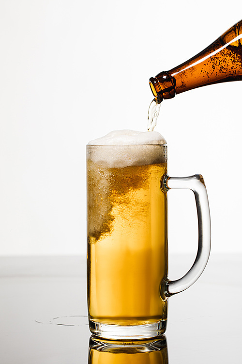 beer pouring from bottle into glass with bubbles isolated on white