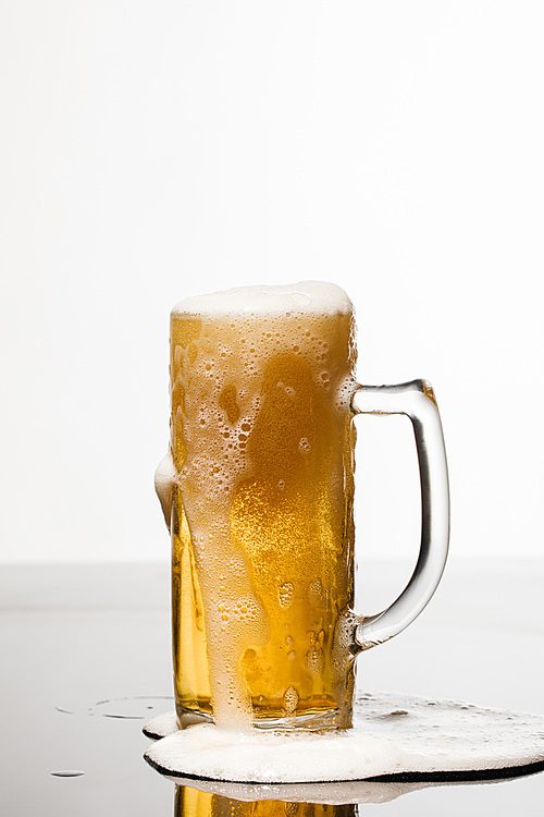 wet glass of beer with foam and puddle on surface isolated on white