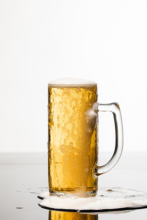 wet glass of beer with foam and spilled puddle on surface isolated on white