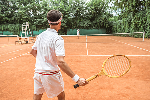 back view of sportsman playing tennis with wooden racket on tennis court