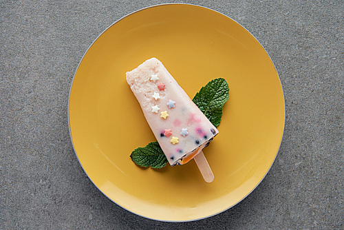 top view of delicious fruity popsicle with green mint leaves on yellow plate on grey