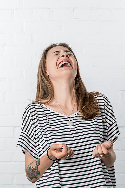 Laughing young woman wearing striped shirt on white brick wall background