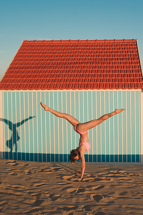 young woman in pink bikini standing on hands against building in Portugal
