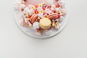 top view of pink cake with marshmallows and macarons on white plate with copy space