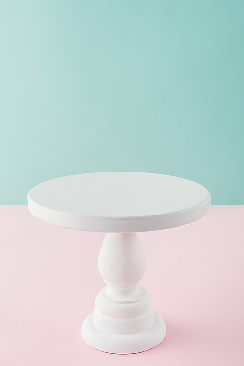 empty white cake stand on pink and turquoise background with copy space