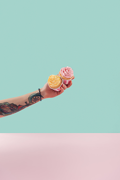 cropped view of tattooed woman holding two cupcakes with buttercream