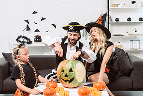 family in halloween costumes on sofa at coffee table with pumpkins at home