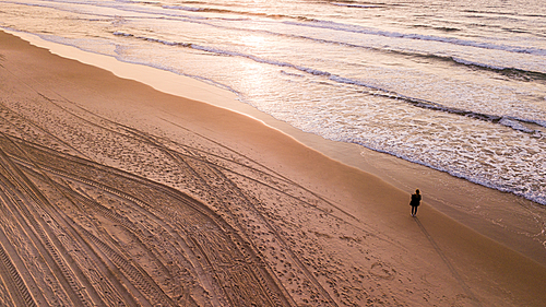 aerial view of lonely woman standing on empty sandy beach and looking at sunset, Ashdod, Israel