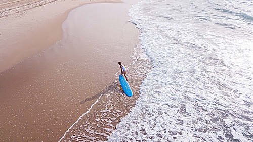 aerial view of young woman in white swimsuit pulling surfboard on sandy beach, Ashdod, Israel