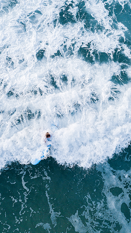 aerial view of woman riding surfboard in stormy blue sea, Ashdod, Israel
