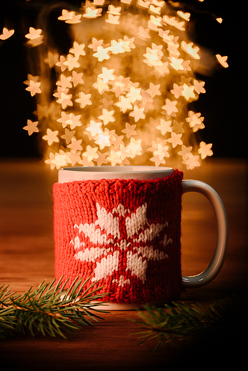 close up view of cup of hot drink and pine tree branches on wooden tabletop with stars bokeh lights background
