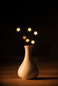 close up view of white vase and yellow stars bokeh lights on black background
