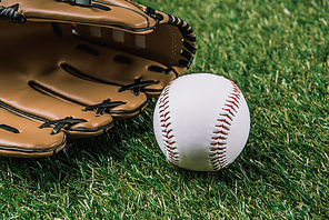 close up view of baseball ball and glove lying on green grass