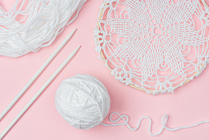 flat lay with white yarn and knitting needles on pink backdrop