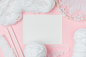 flat lay with white yarn, knitting needles and blank paper on pink background