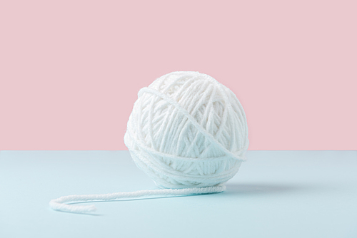 close up view of white yarn ball on blue and pink background