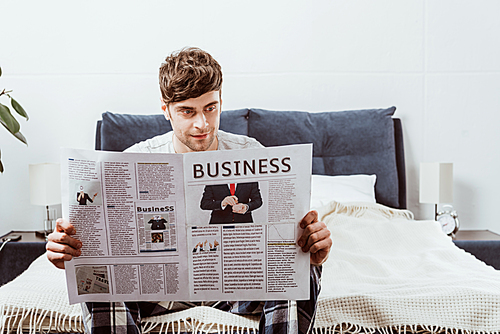 smiling man reading business newspaper on bed at home