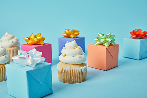 Delicious cupcakes and colorful gifts on blue background