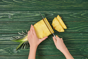 cropped view of woman cutting yellow ripe pineapple on green wooden table