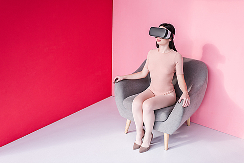 beautiful girl in bodysuit and high heeled shoes using virtual reality headset while sitting on chair