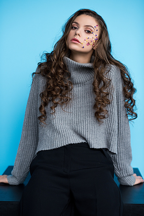 attratcive young woman with flowers on face in stylish sweater sitting on table