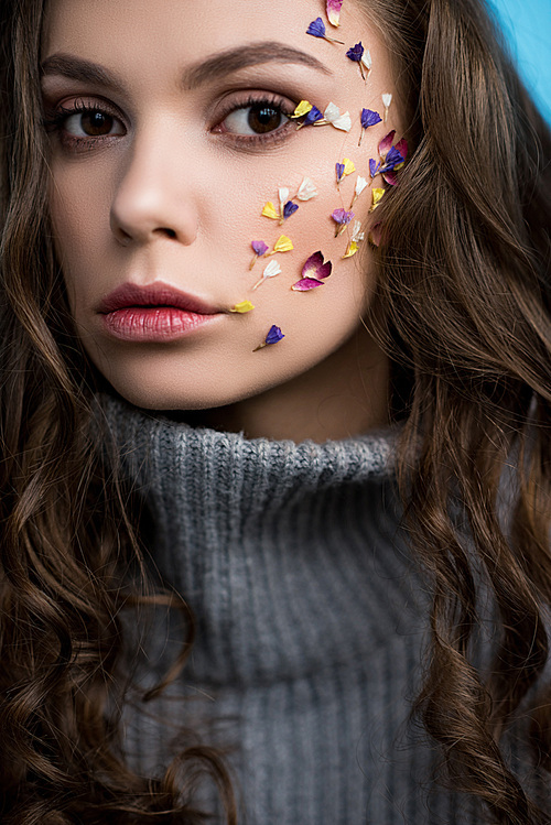 close-up portrait of stylish young woman with flowers on face in grey knitted turtleneck sweater