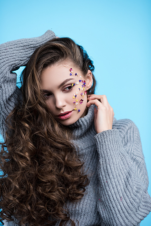 attractive young woman with flowers on face in warm knitted sweater isolated on blue