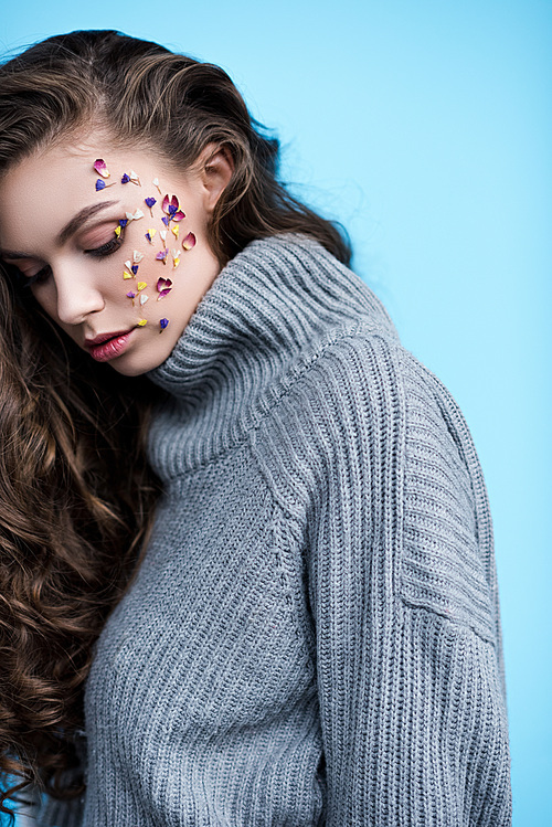 attractive young woman with flowers on face in warm grey sweater isolated on blue