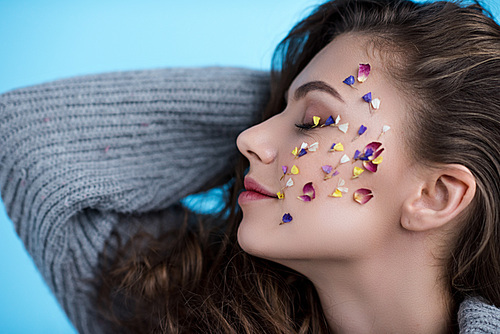 happy young woman with flowers on face in warm sweater isolated on blue