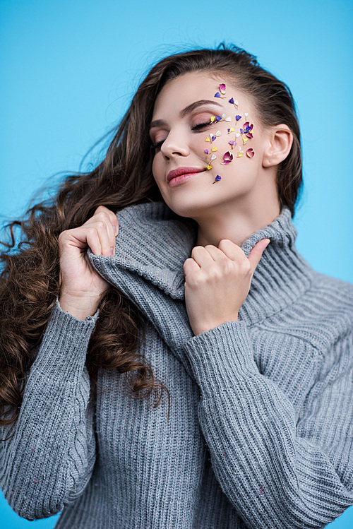 woman with flowers on face stretching neck of stylish sweater isolated on blue